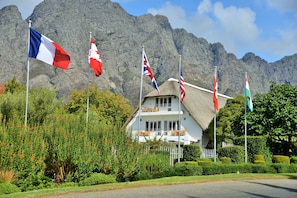 A white building with a thatched roof, surrounded by lush greenery and mountains in the background. - Le Franschhoek Hotel and Spa by Dream Resorts  (Franschhoek)