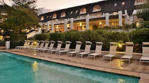 A pool area with lounge chairs and a building with arched windows in the background. - Le Franschhoek Hotel and Spa by Dream Resorts  (Franschhoek)