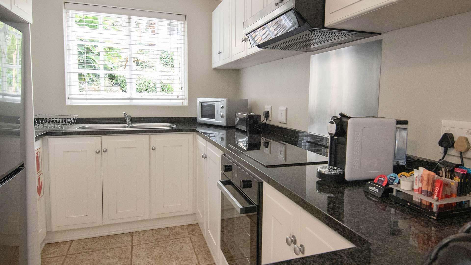 A modern kitchen with white cabinets, a black countertop, a microwave, a coffee maker, and a window with blinds.