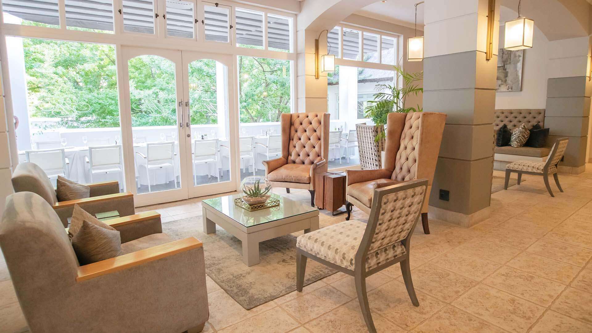 A spacious living area with a glass coffee table, comfortable seating, and large windows offering a view of the outdoors.