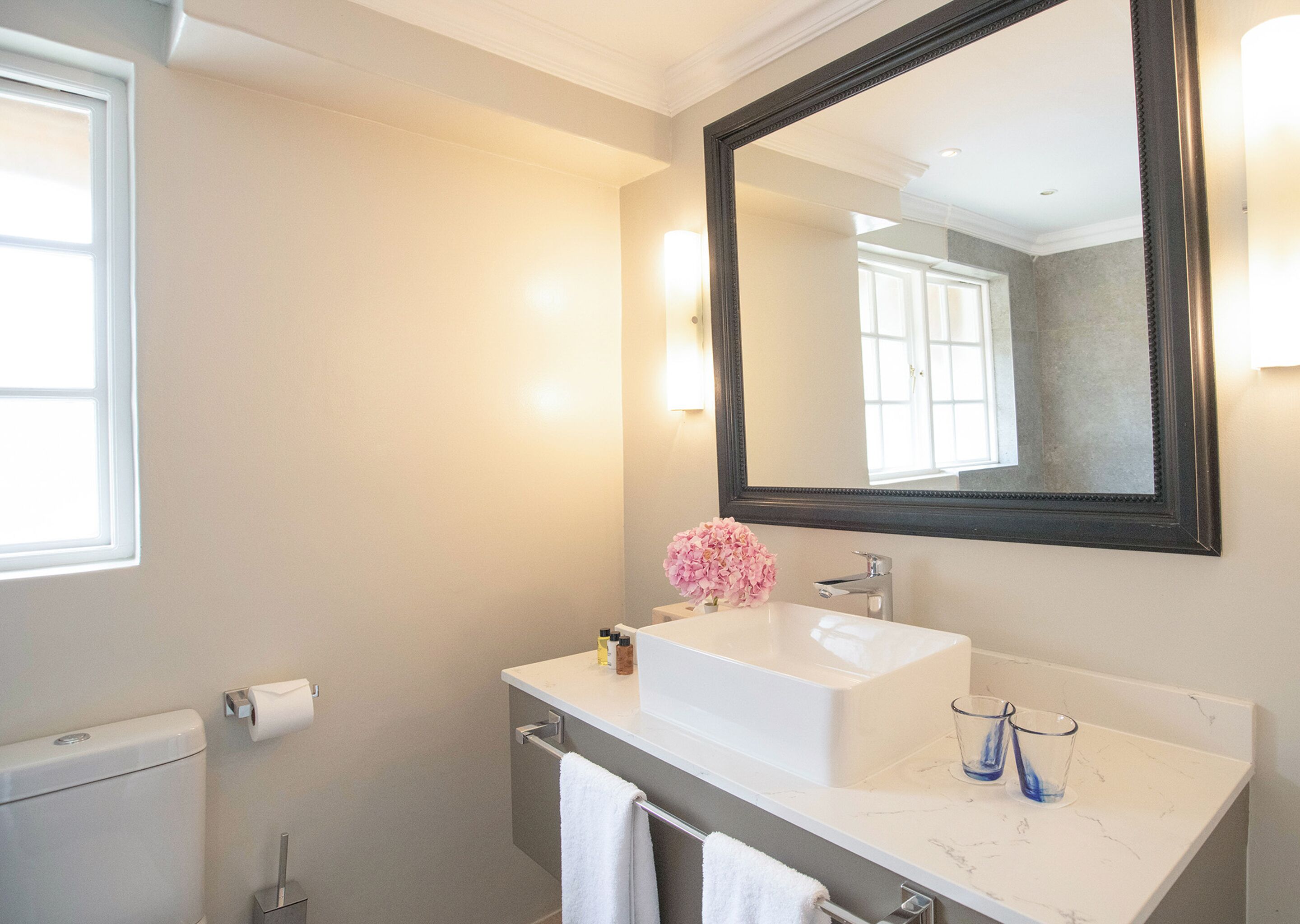 A bathroom with a white sink, a large mirror, a towel rack, and a window.