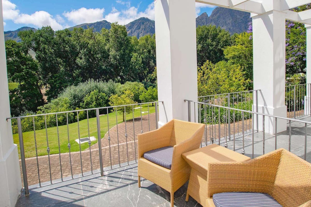 A balcony with wicker furniture and a view of a lush garden and mountains.