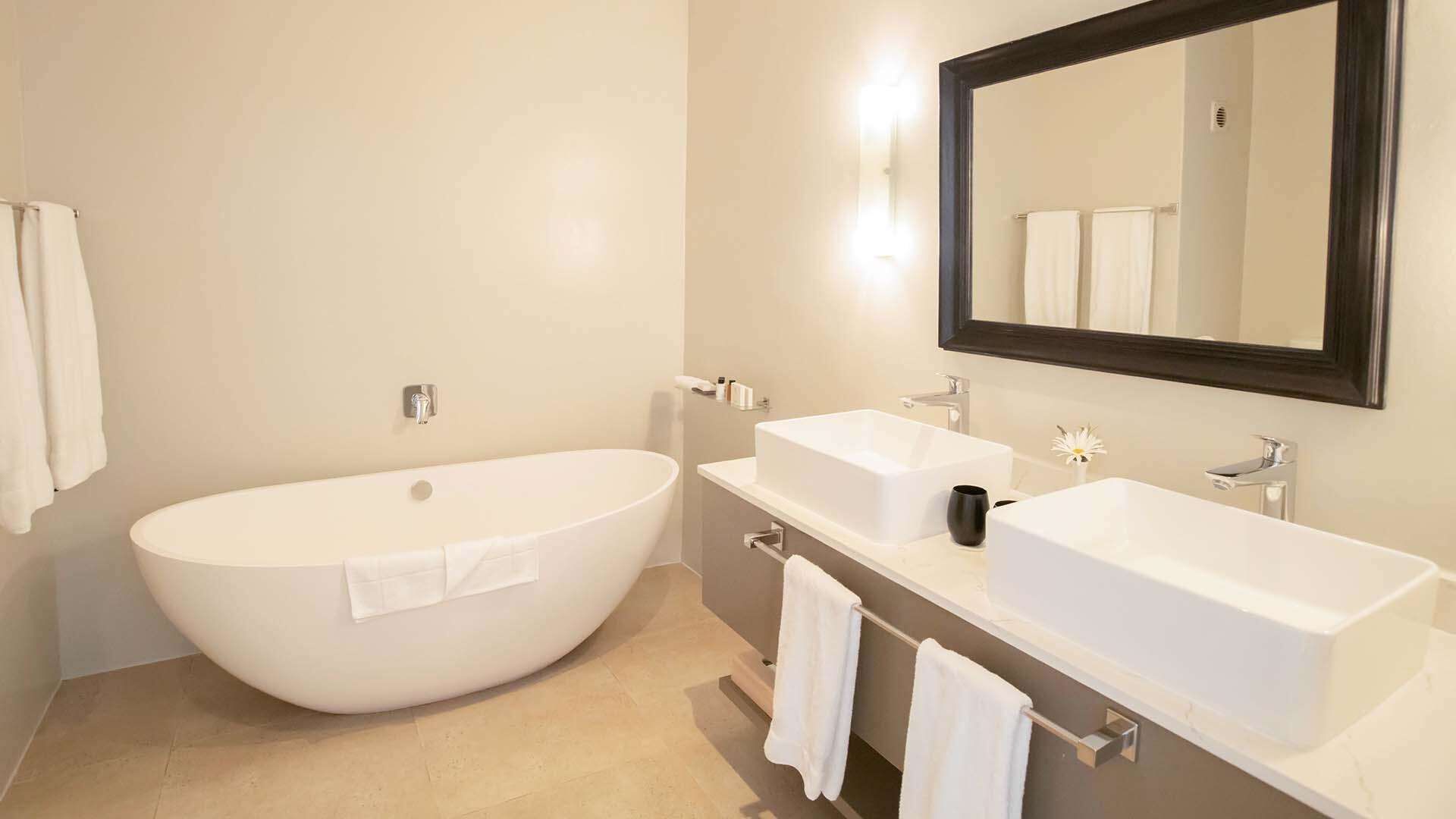 A modern bathroom with a freestanding bathtub, two sinks, and a large mirror.
