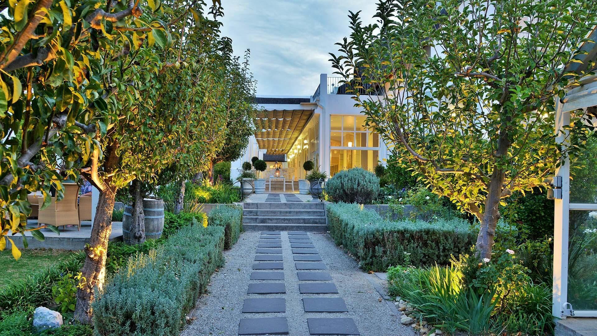 A pathway leading to a building with a modern design, surrounded by well-maintained gardens and trees.
