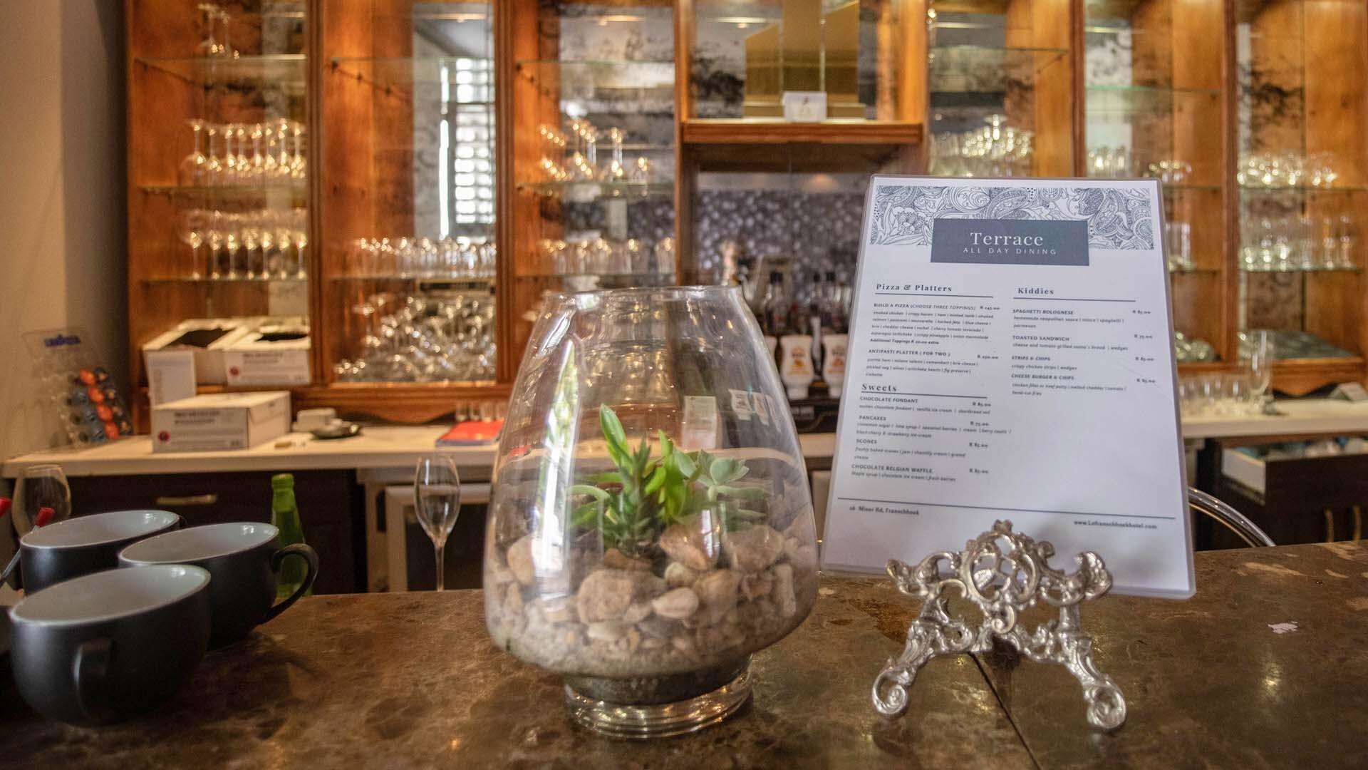 Un cartel de menú con el título 'Terrace All Day Dining', que incluye secciones para pizzas y tablas para compartir, opciones infantiles y postres.