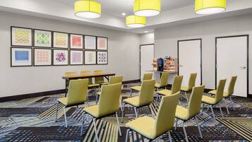 Une salle de conférence avec des chaises jaunes, une table et des œuvres d’art encadrées accrochées au mur.