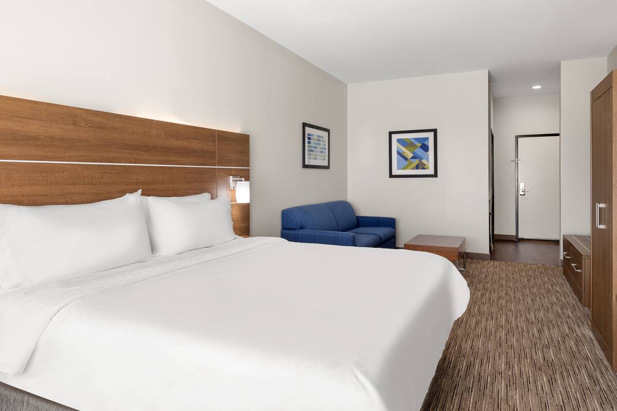 Ein Hotelzimmer mit einem großen Bett, einem blauen Sessel, einem Holz-Kopfschild und einem gerahmten Bild an der Wand.