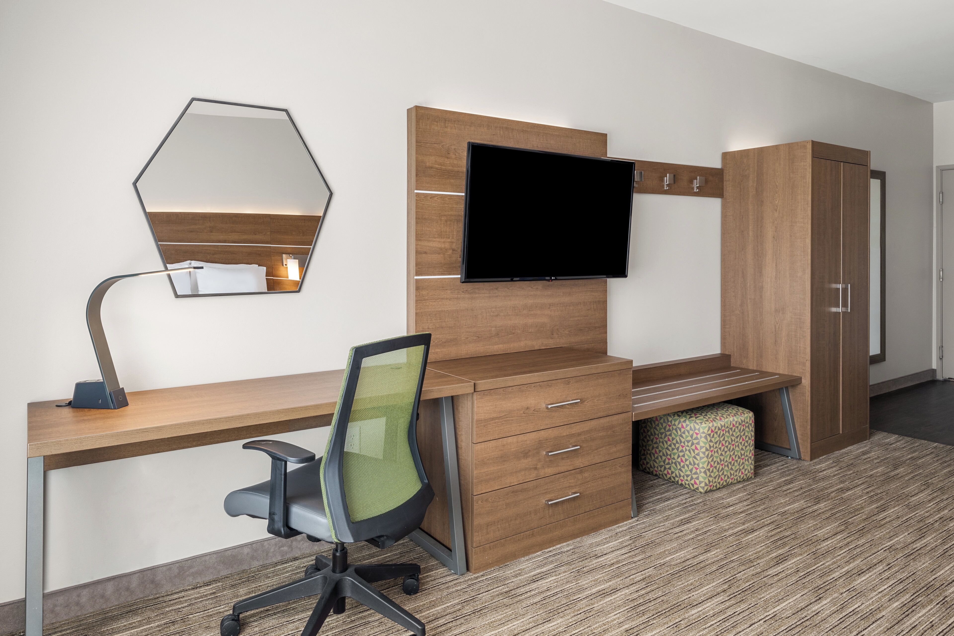 Habitación de hotel con escritorio de madera, una silla, televisor de pantalla plana, espejo y armario.