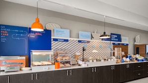Un espace dédié au petit-déjeuner, équipé d’un écran numérique, d’un présentoir de viennoiseries et d’un panneau indiquant que le petit-déjeuner est prêt.