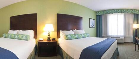 A hotel room with two beds, a nightstand with a lamp, a window with curtains, and a framed picture on the wall.