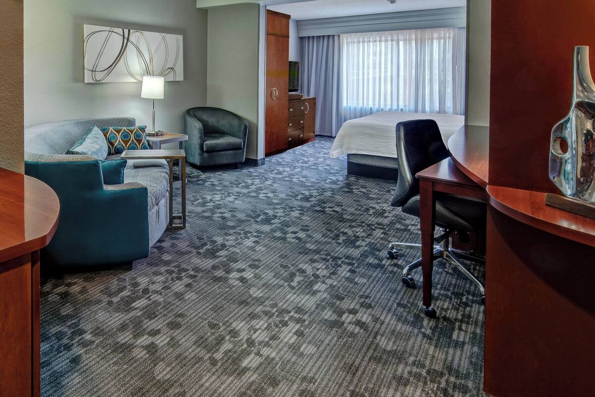 A hotel room with a sofa, a chair, a desk, a bed, and a large window with curtains.