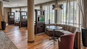 A modern hotel lobby with wooden flooring, a large sofa, a round table, and two televisions mounted on dark wooden panels. - Courtyard by Marriott Troy (Troy)