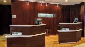 A reception area with two wooden reception desks, a sign indicating it's for employees only, and a decorative wall piece above the desks. - Courtyard by Marriott Troy (Troy)