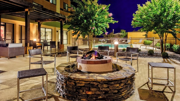 An outdoor seating area with a stone fire pit, surrounded by chairs and a pool in the background. - Courtyard by Marriott Troy (Troy)