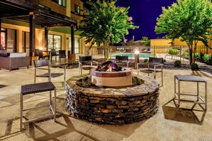An outdoor seating area with a stone fire pit, surrounded by chairs and a pool in the background. - Courtyard by Marriott Troy (Troy)