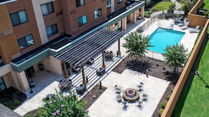 An outdoor pool area with a covered seating area, a fire pit, and a well-maintained lawn. - Courtyard by Marriott Troy (Troy)