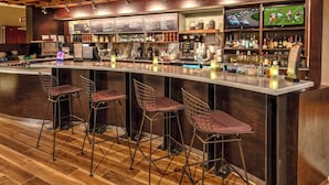A bar area with a long counter, bar stools, and a television screen displaying a football game. - Courtyard by Marriott Troy (Troy)