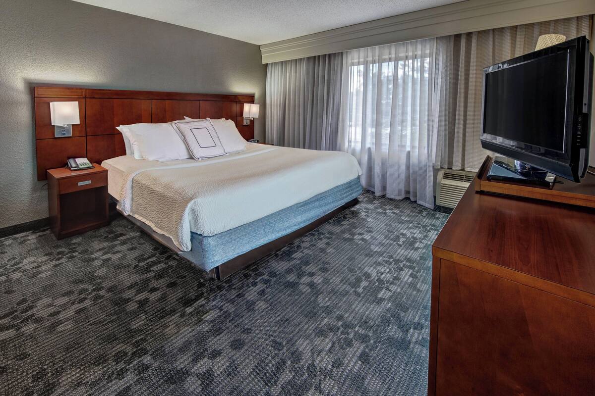 A hotel room with a large bed, a wooden headboard, a television, and a desk with a lamp.