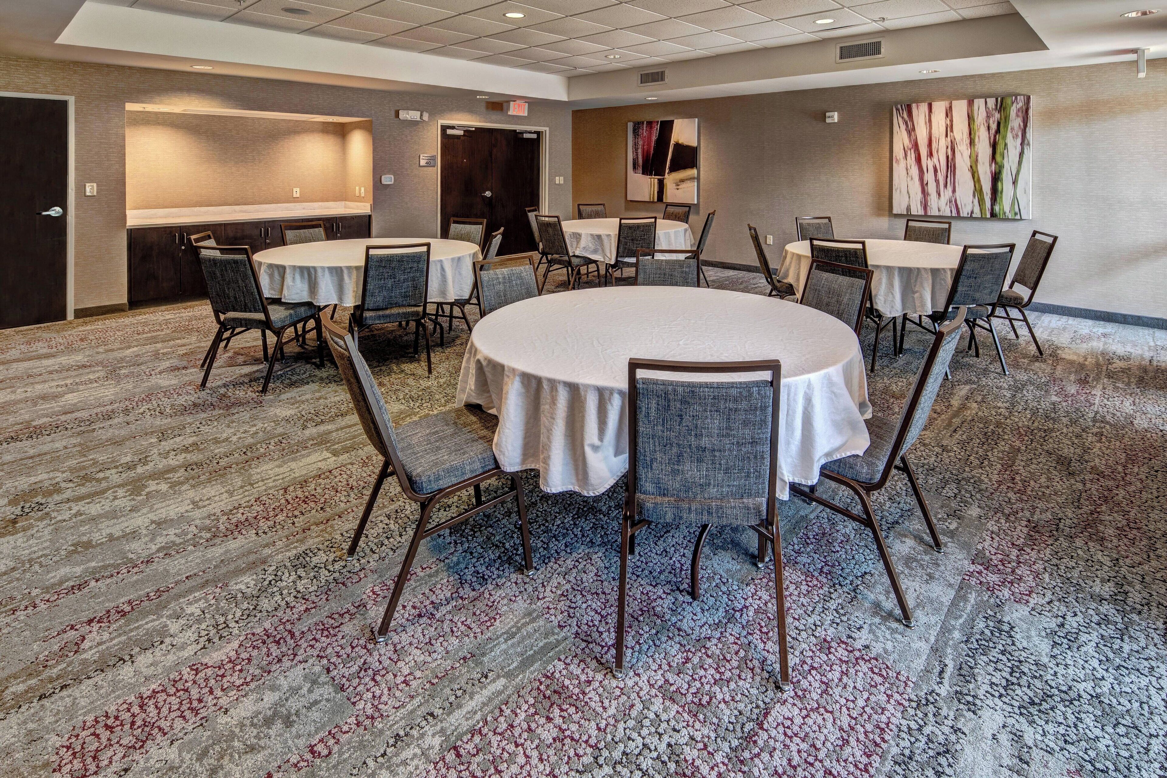 A conference room with round tables and chairs, carpeted flooring, and a large abstract painting on the wall.