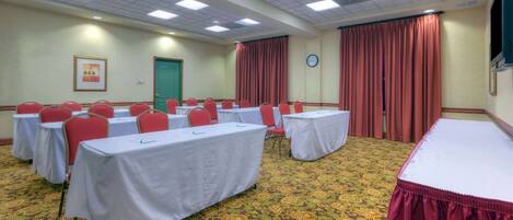 A conference room with tables and chairs, a patterned carpet, a clock, and a green door.