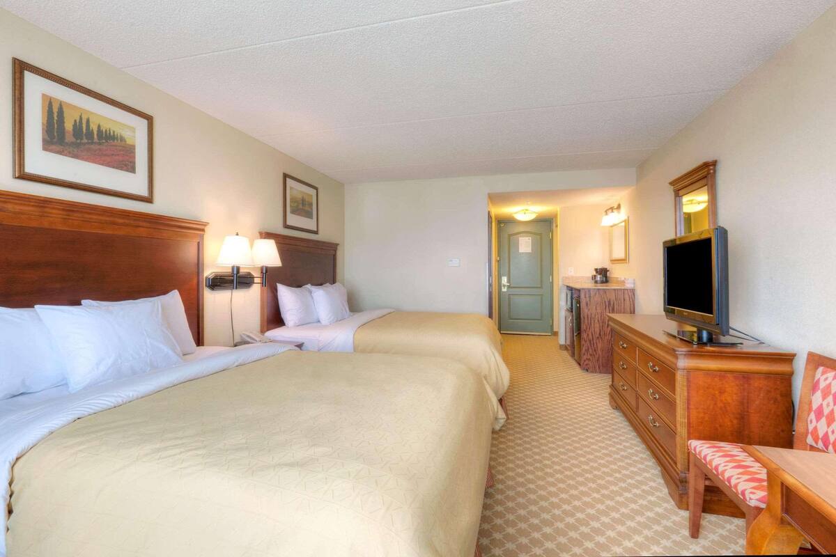 Une chambre d’hôtel avec deux lits, une télévision, une commode et un bureau avec une chaise.