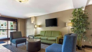 A modern hotel lobby with a green sofa, blue armchairs, a round coffee table, a flat-screen TV, and a large potted plant. - Quality Inn Raleigh Downtown (Raleigh)