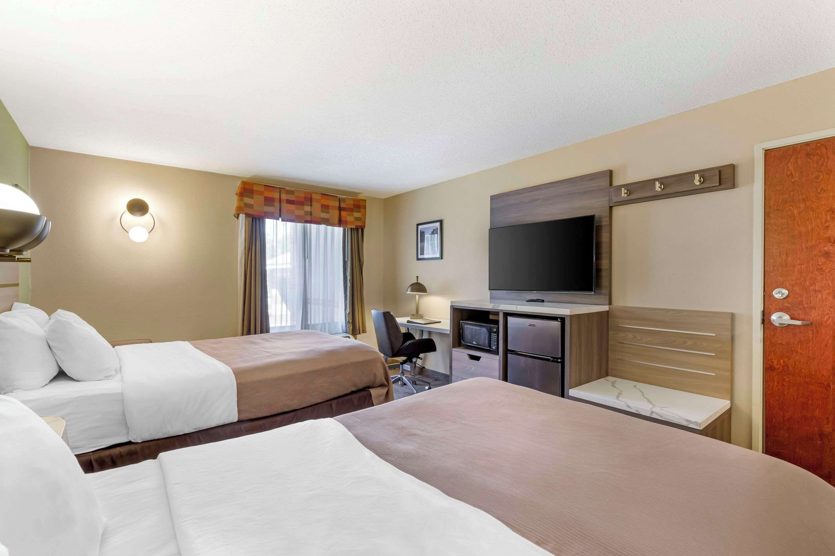 A hotel room with two beds, a desk with a computer, a television, and a minibar.