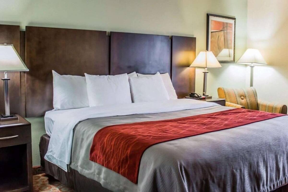 A hotel room with a bed, two bedside lamps, a chair, and a painting on the wall.