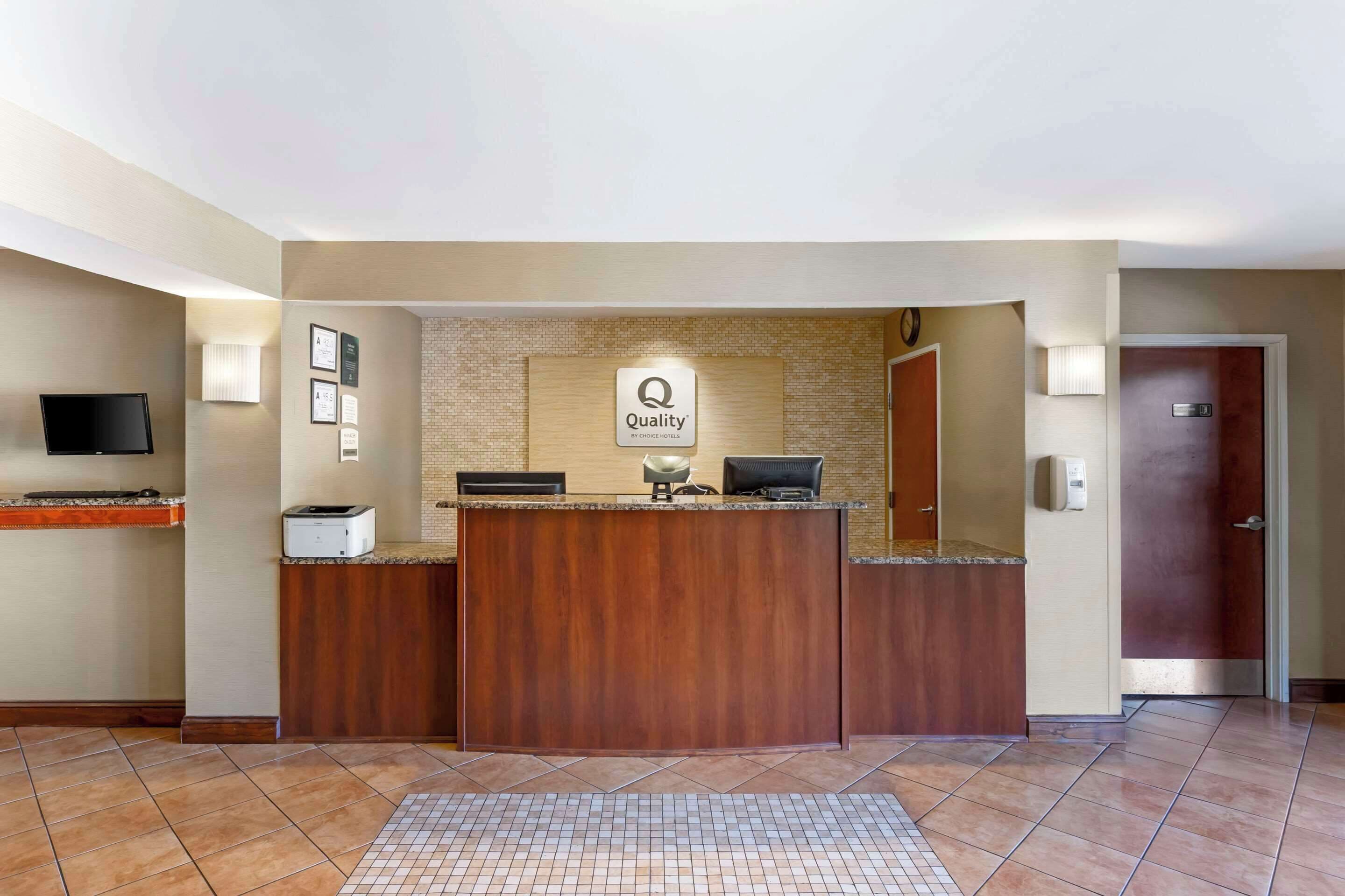 A reception desk with a 'Quality' sign, a flat-screen TV, and a printer.