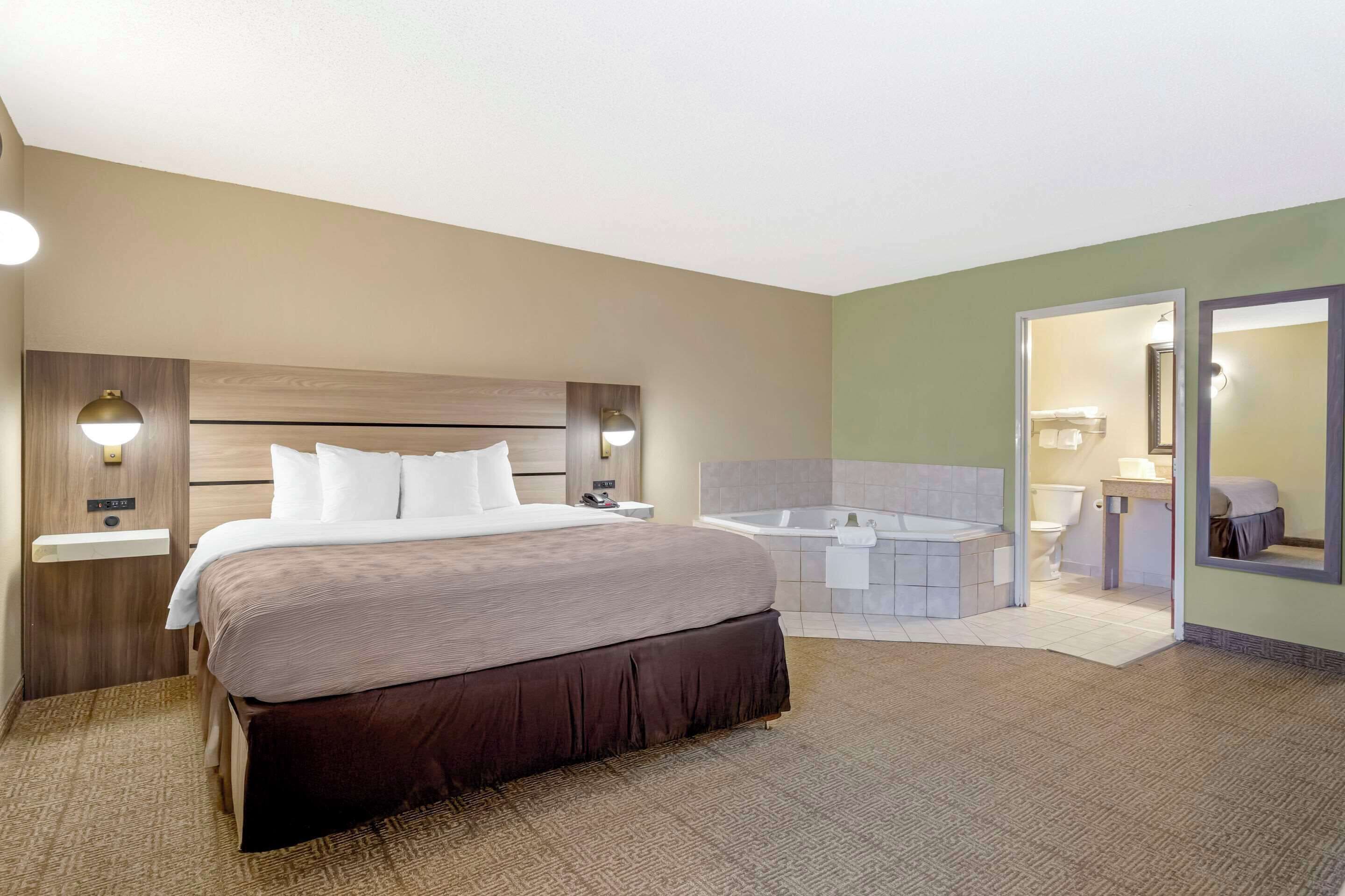 Een hotelkamer met een groot bed, een aparte badkamer met bad en een spiegel.