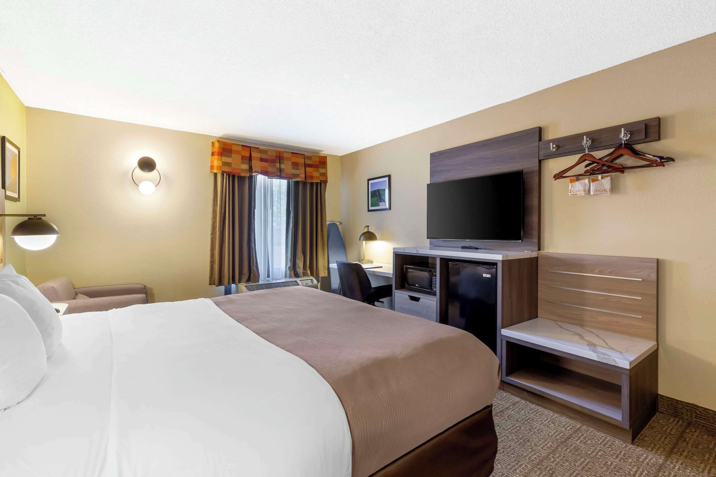 A hotel room with a large bed, a desk with a computer, a television, and a seating area with a chair.