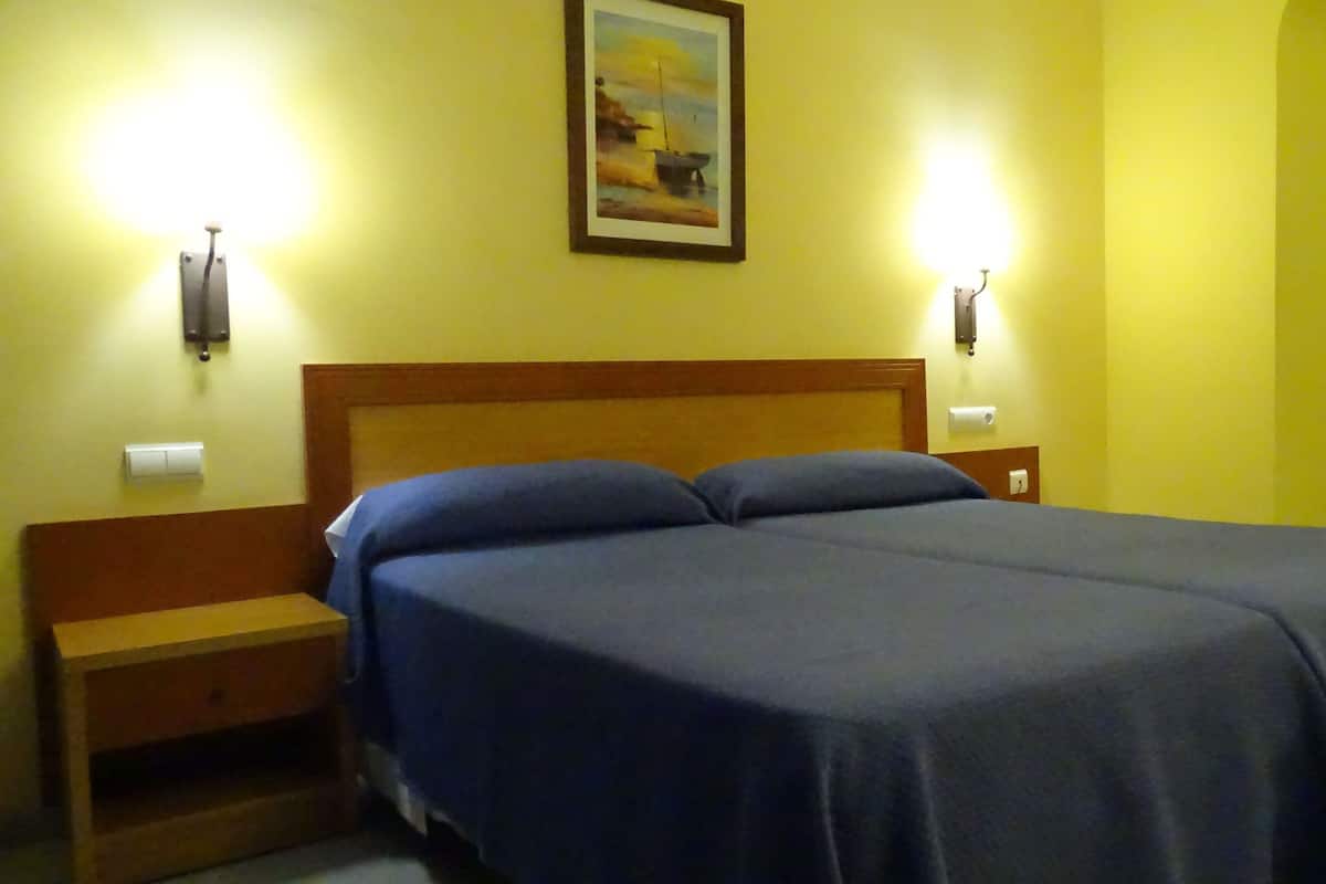 A hotel room with a bed, two bedside tables, and two wall-mounted lamps.