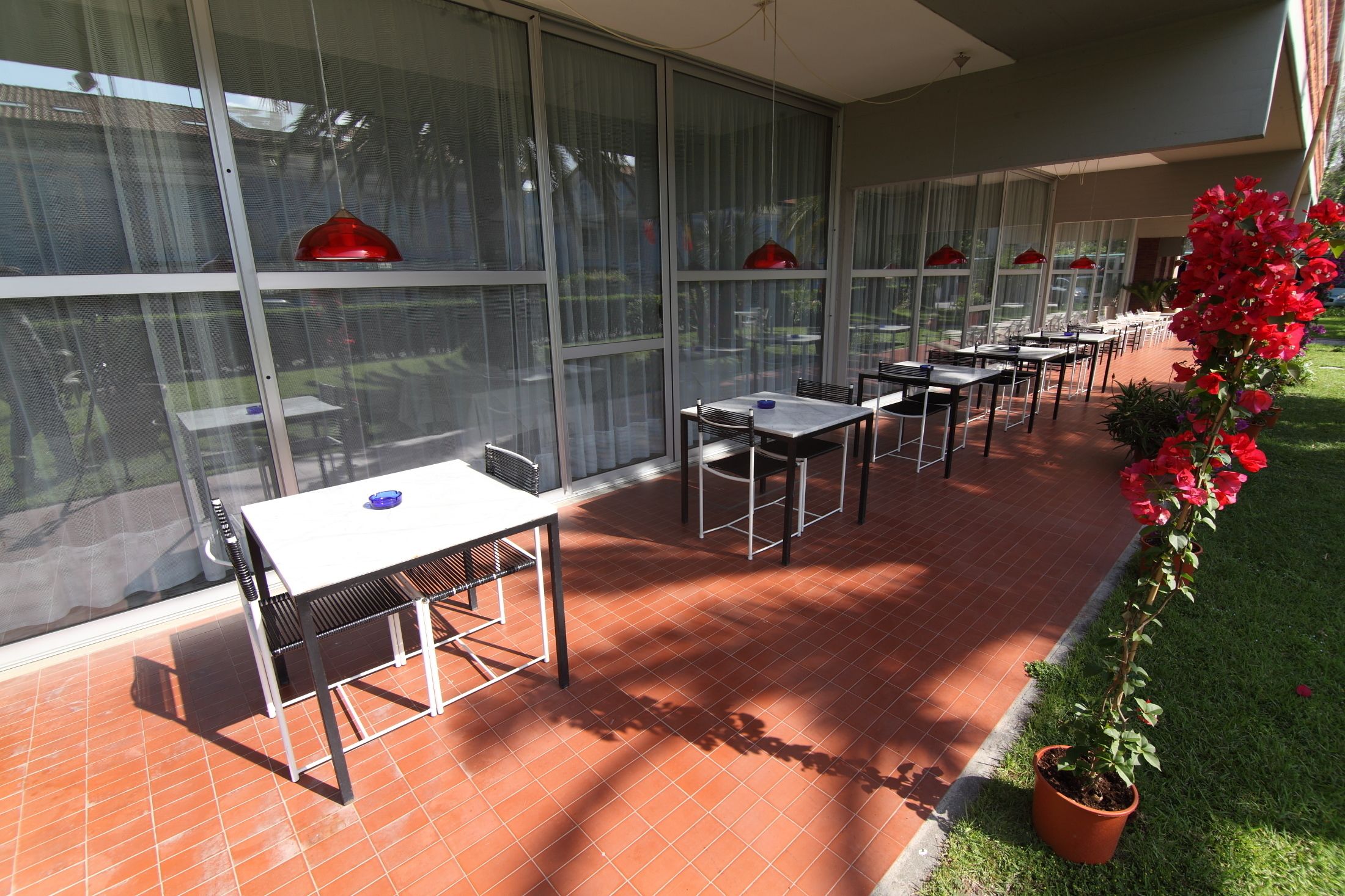 Una terrazza esterna con tavoli e sedie, ampie finestre e una pianta in vaso.