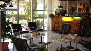 A spacious lounge area with multiple seating options, a bar area with a variety of bottles, and large windows offering a view of the outdoors. - Hotel Marina (Massa)
