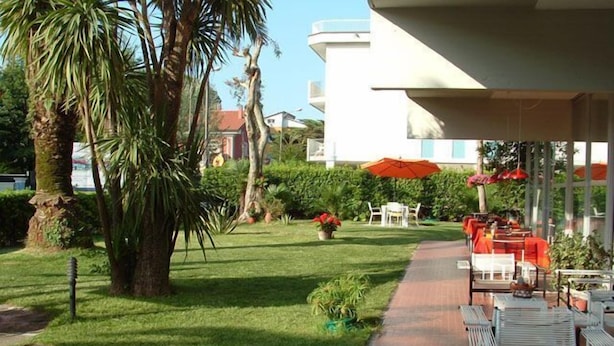 A patio area with outdoor seating, a pathway, and a building in the background. - Hotel Marina (Massa)