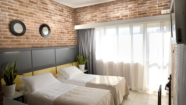 A hotel room with two beds, a brick wall, a large window with curtains, and a potted plant. - Hotel Marina (Massa)
