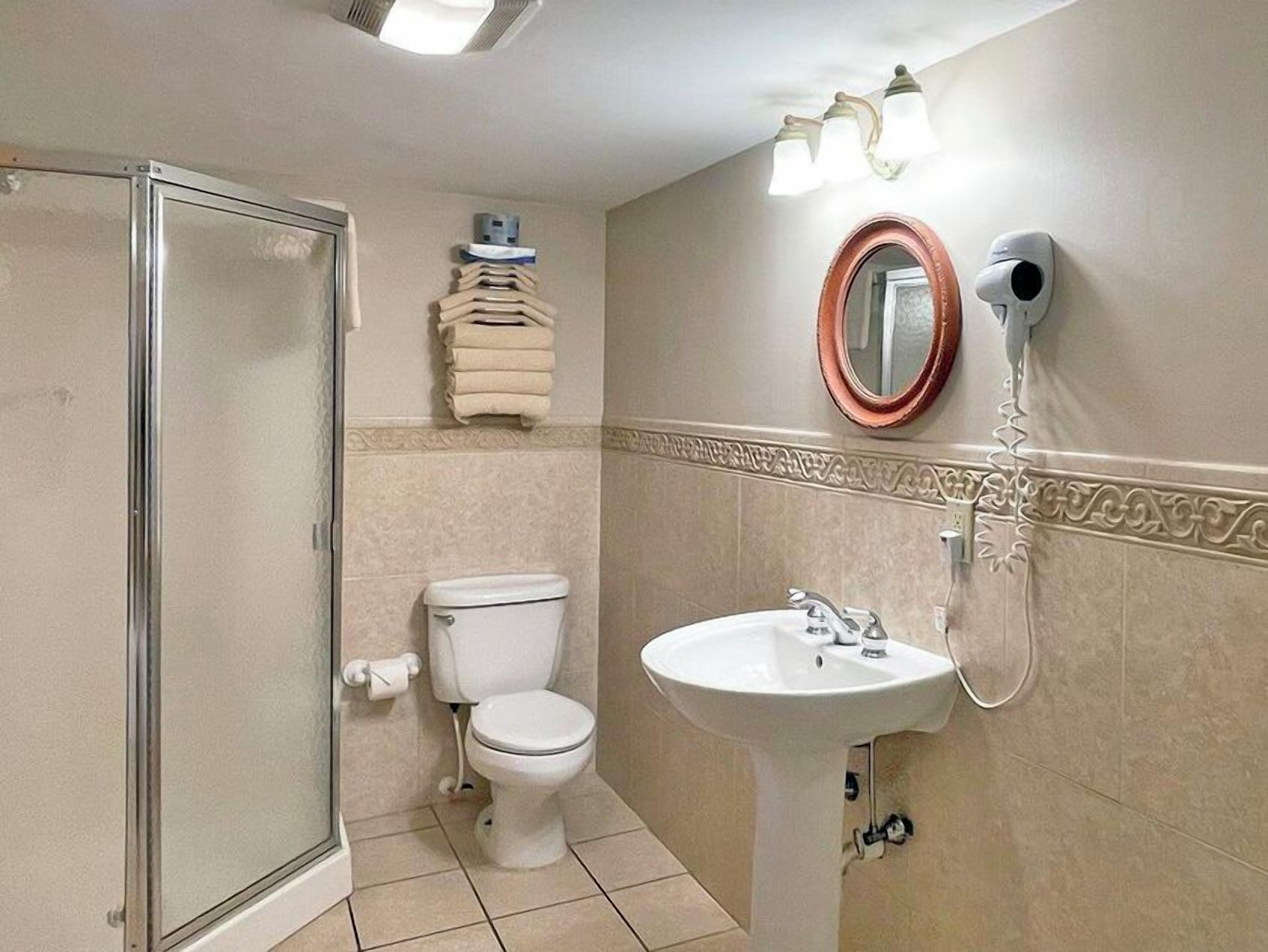 Une salle de bain équipée de toilettes, d’un lavabo et d’une douche. On y trouve un porte-serviettes au-dessus des toilettes et un sèche-cheveux fixé au mur.