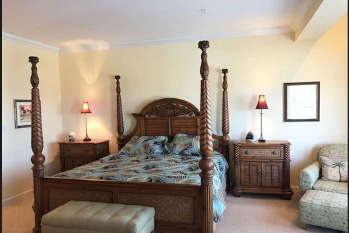 Een slaapkamer met een hemelbed, twee nachtkastjes, een bankje, een stoel en een kaptafel.