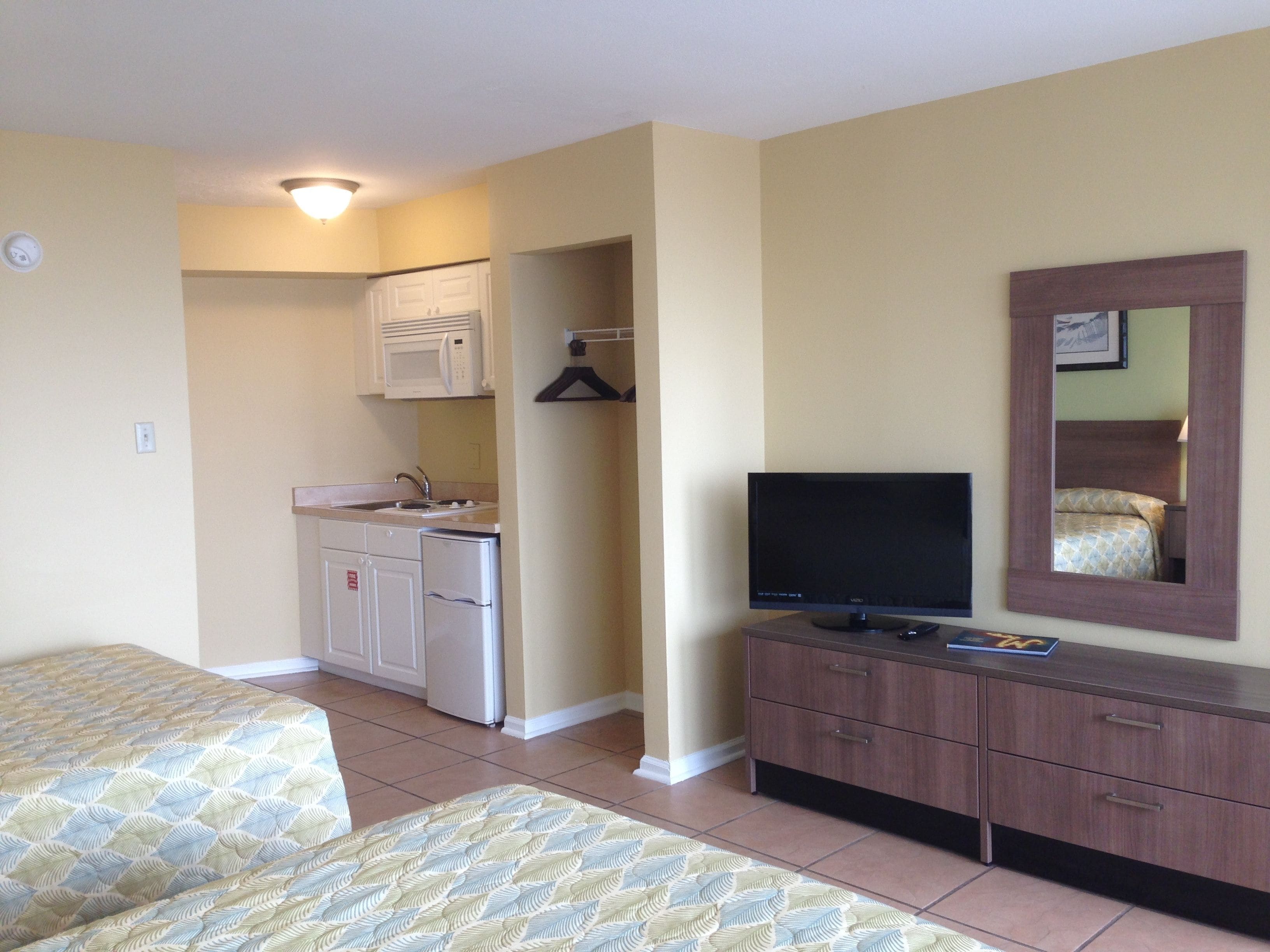 A hotel room with a kitchenette, a TV, a bed, and a dresser.