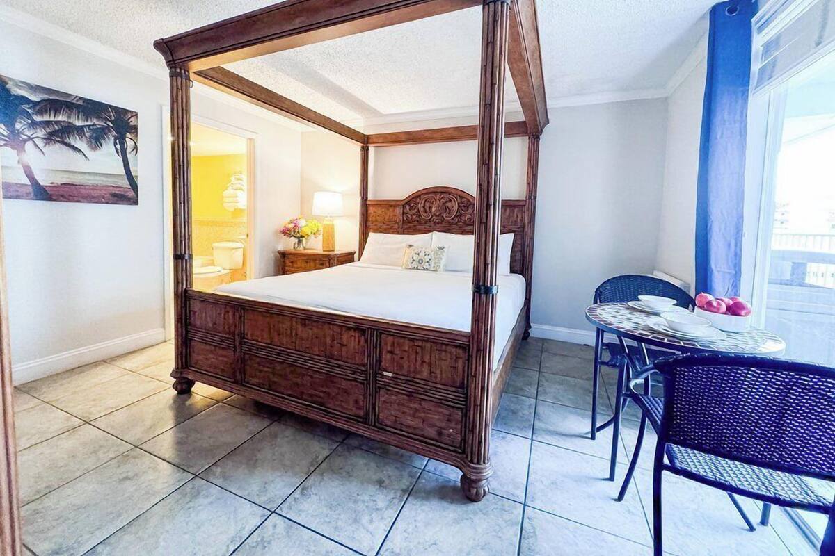 Een hemelbed met een houten hoofdbord, een klein tafeltje met stoelen en uitzicht buiten door een raam.