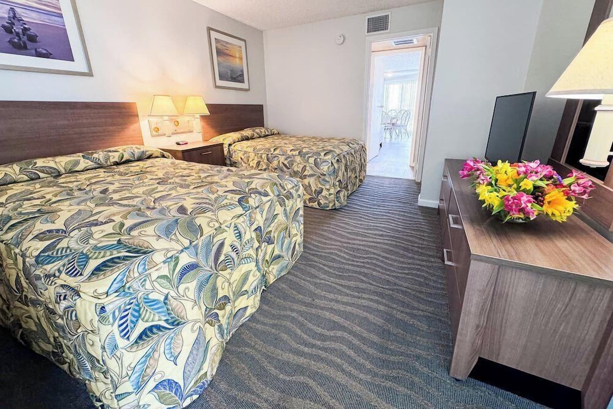 Een hotelkamer met twee bedden, een bureau met lamp, een televisie en een bloemenarrangement.