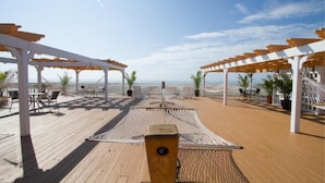 Une terrasse en bois avec des sièges d’extérieur, un hamac et une vue sur la mer.
