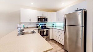 A modern kitchen with white cabinets, stainless steel appliances, and a granite countertop. - Maui Kamaole (Kihei)