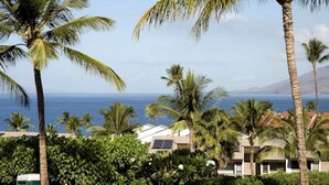 A coastal hotel with palm trees, a view of the ocean, and a mountainous backdrop. - Maui Kamaole (Kihei)