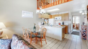 A modern kitchen with wooden cabinets, a central island, and a dining area with wicker chairs.