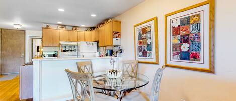 A modern kitchen with wooden cabinets, a central island, and a dining area with a glass table and chairs.