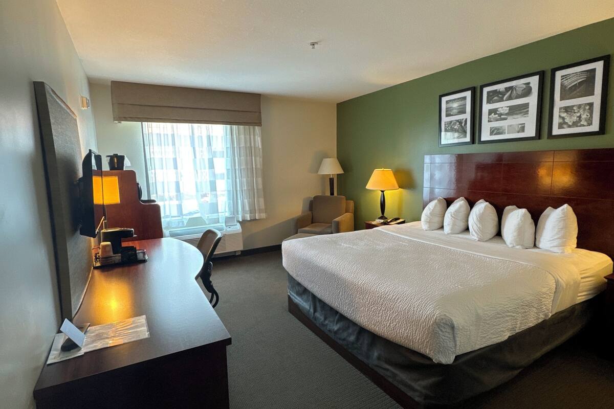 A hotel room with a bed, desk, chair, and a window with curtains.