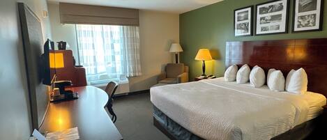 Habitación de hotel con cama, escritorio, silla y ventana con cortinas.