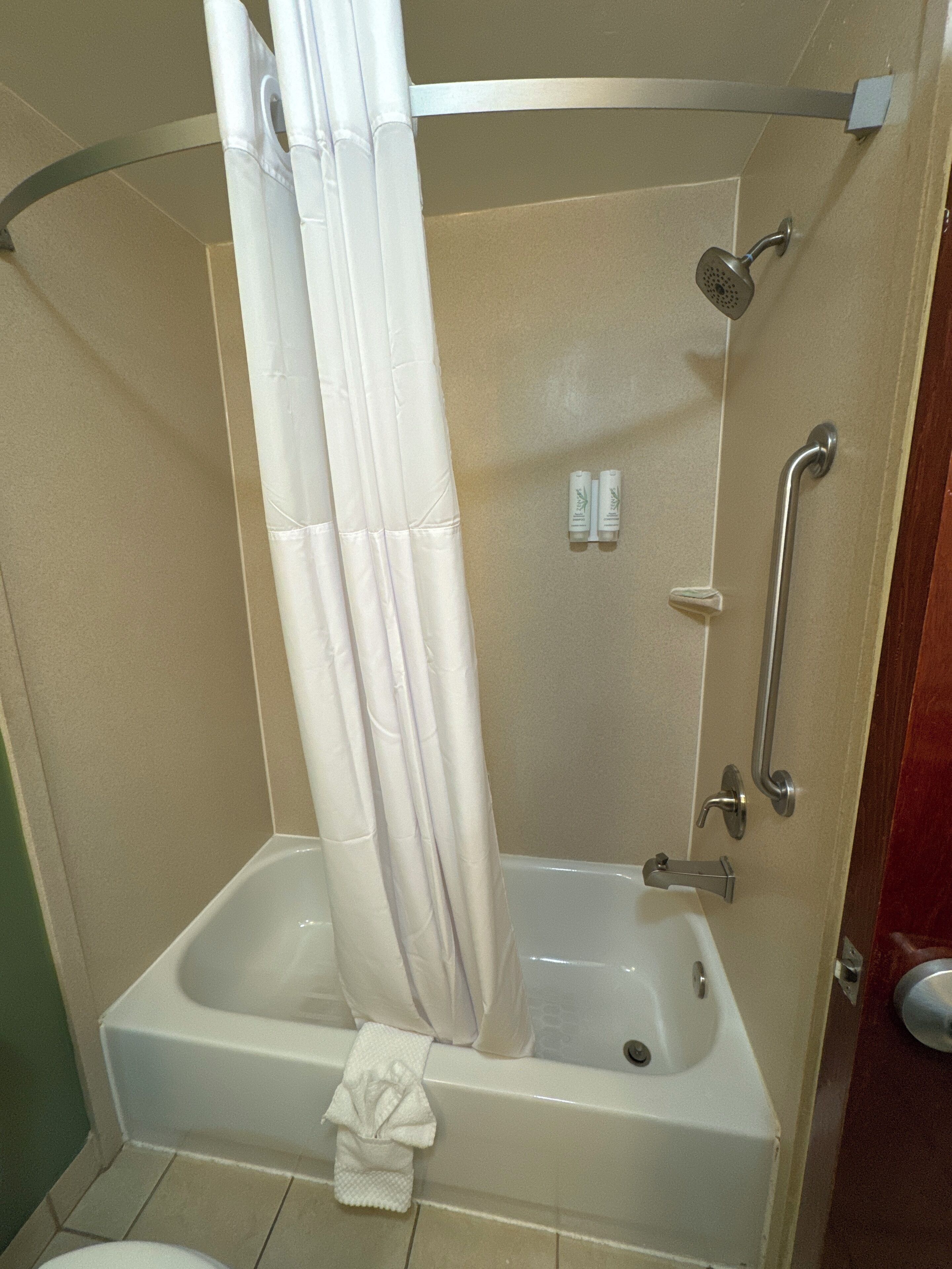 A walk-in shower with a bathtub, grab bars, and a towel rack.