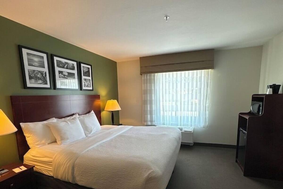 A hotel room with a large bed, two bedside lamps, a desk with a chair, and a window with curtains.